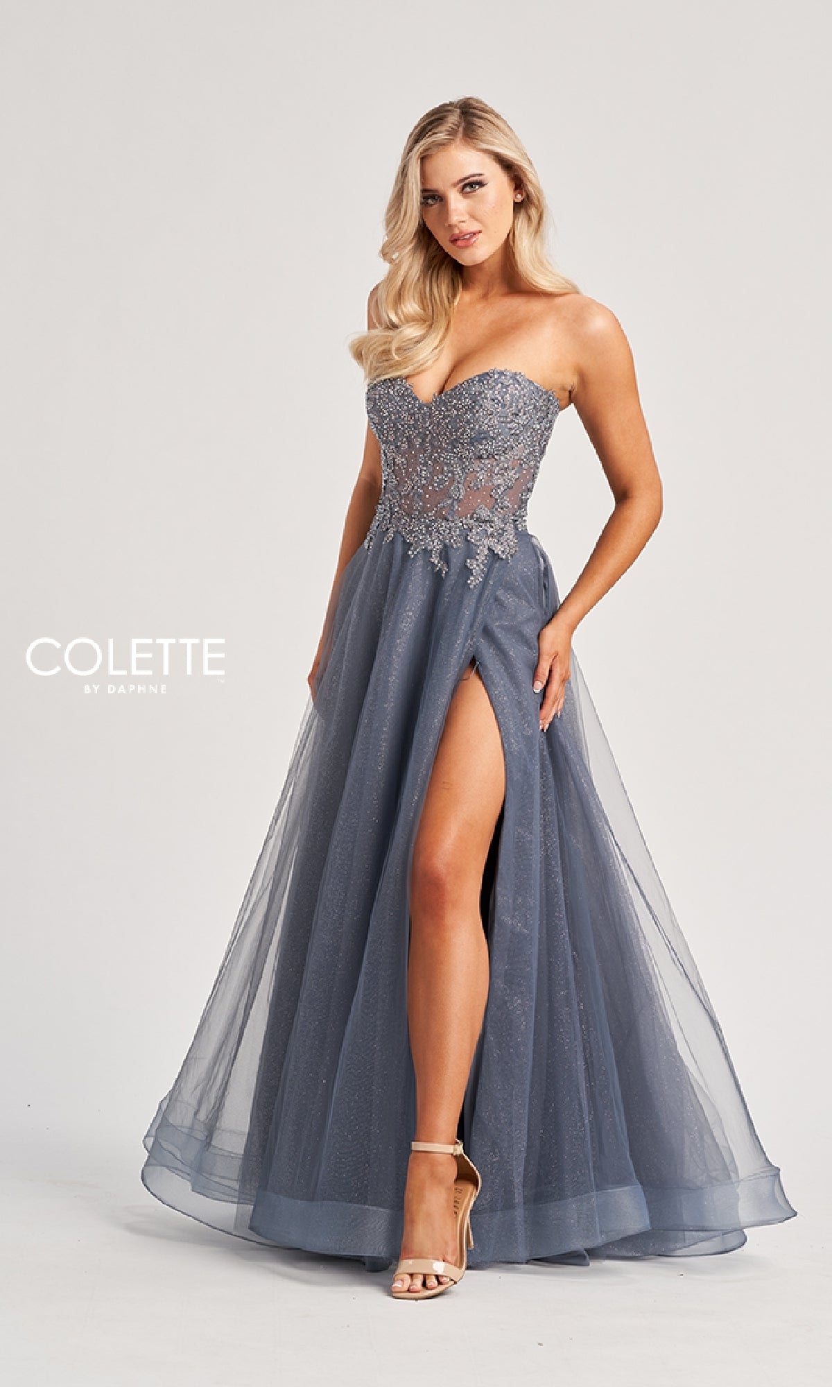 A woman models the Colette CL8110 Long Prom Dress—strapless with an embroidered corset bodice, floral details, a slate blue floor-length A-line skirt, and high slit—posed against a plain backdrop.